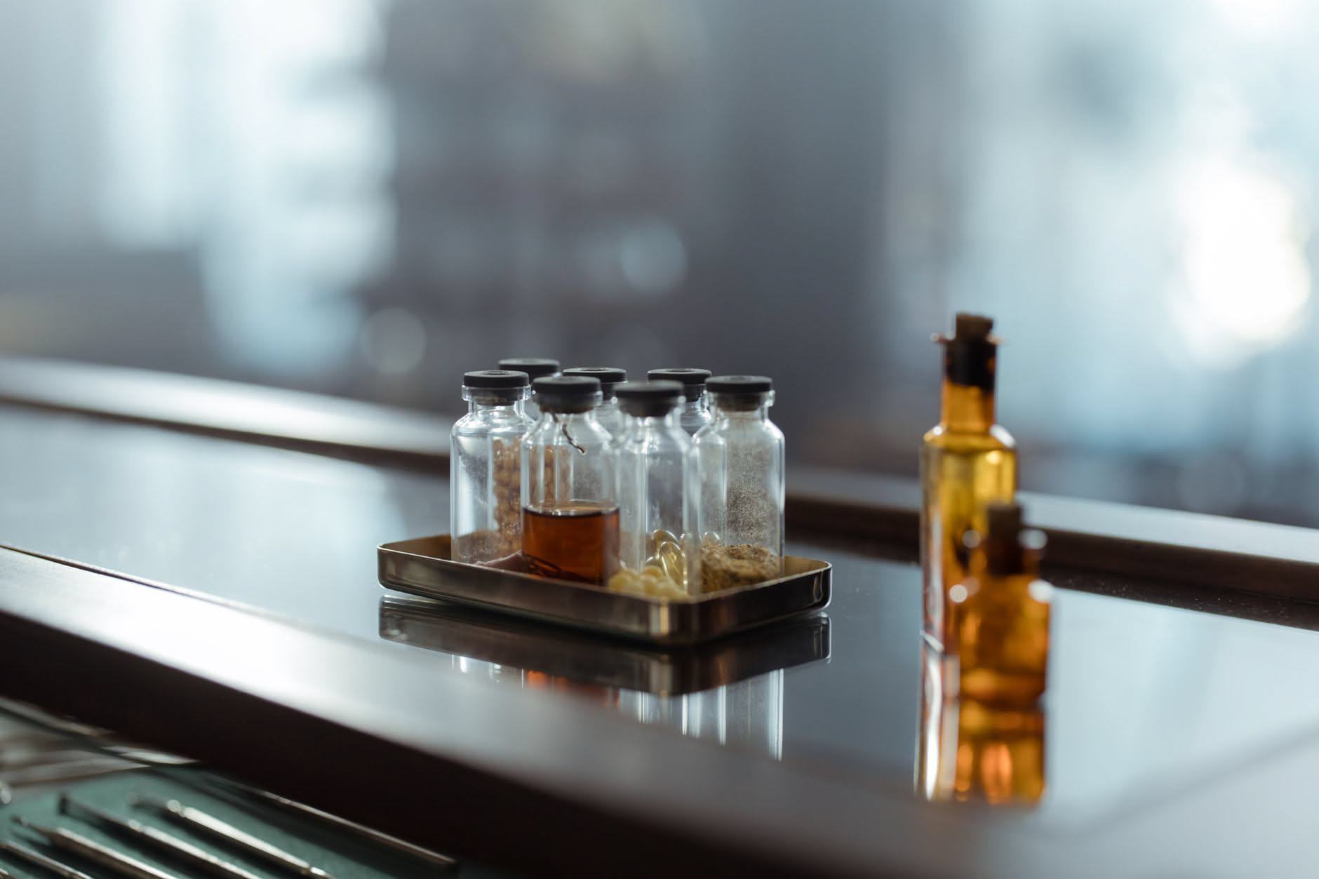 Diverse bottiglie di profumo colorate riposto su uno scaffale in legno naturale con luce naturale diffusa, accanto a specchi e accessori per la bellezza