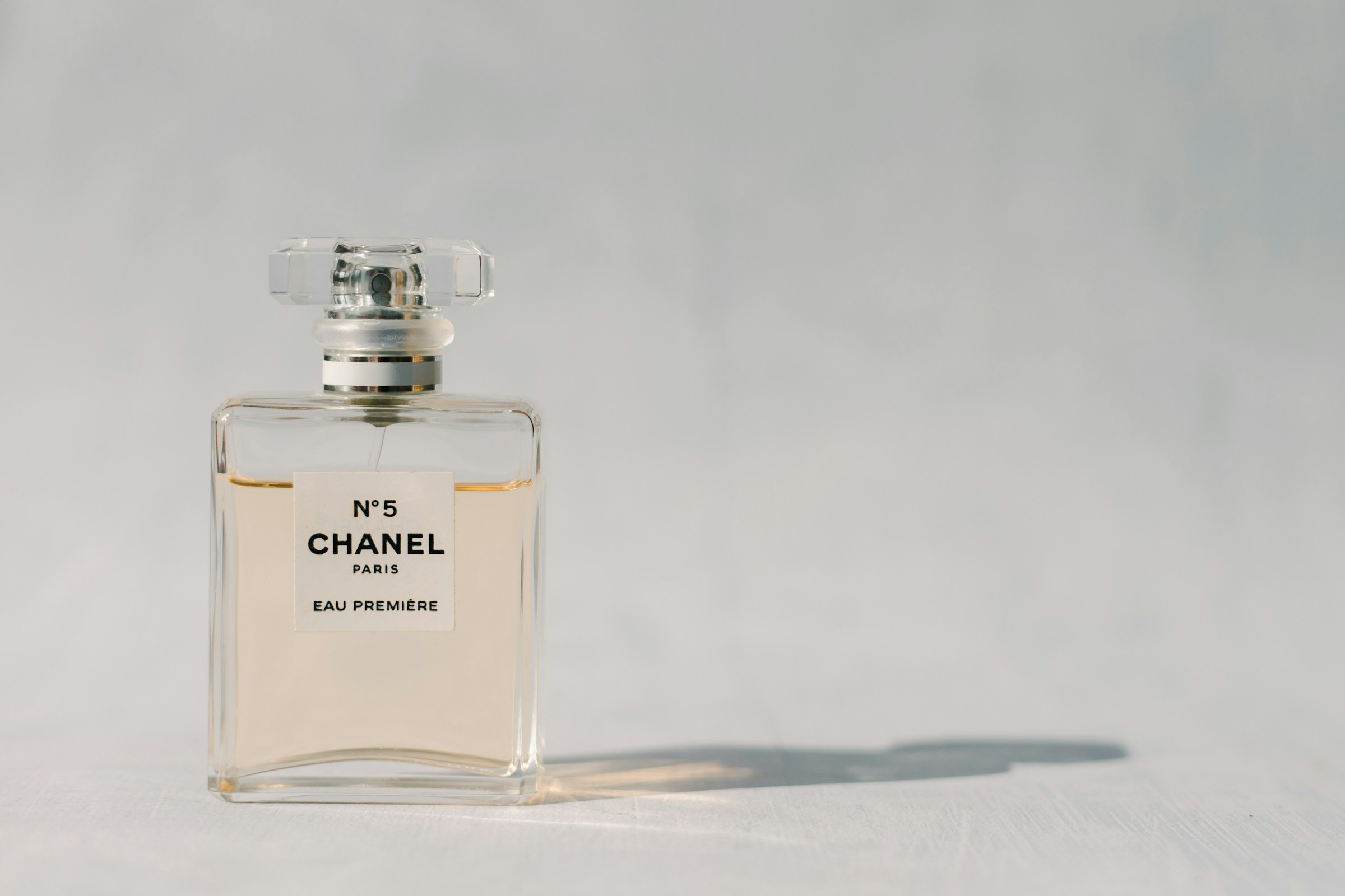 Selezione di flaconi di profumo di diverse dimensioni e marche, alcuni lussuosi con tappi decorativi, altri minimal, disposti su superficie riflettente con luci sfumate