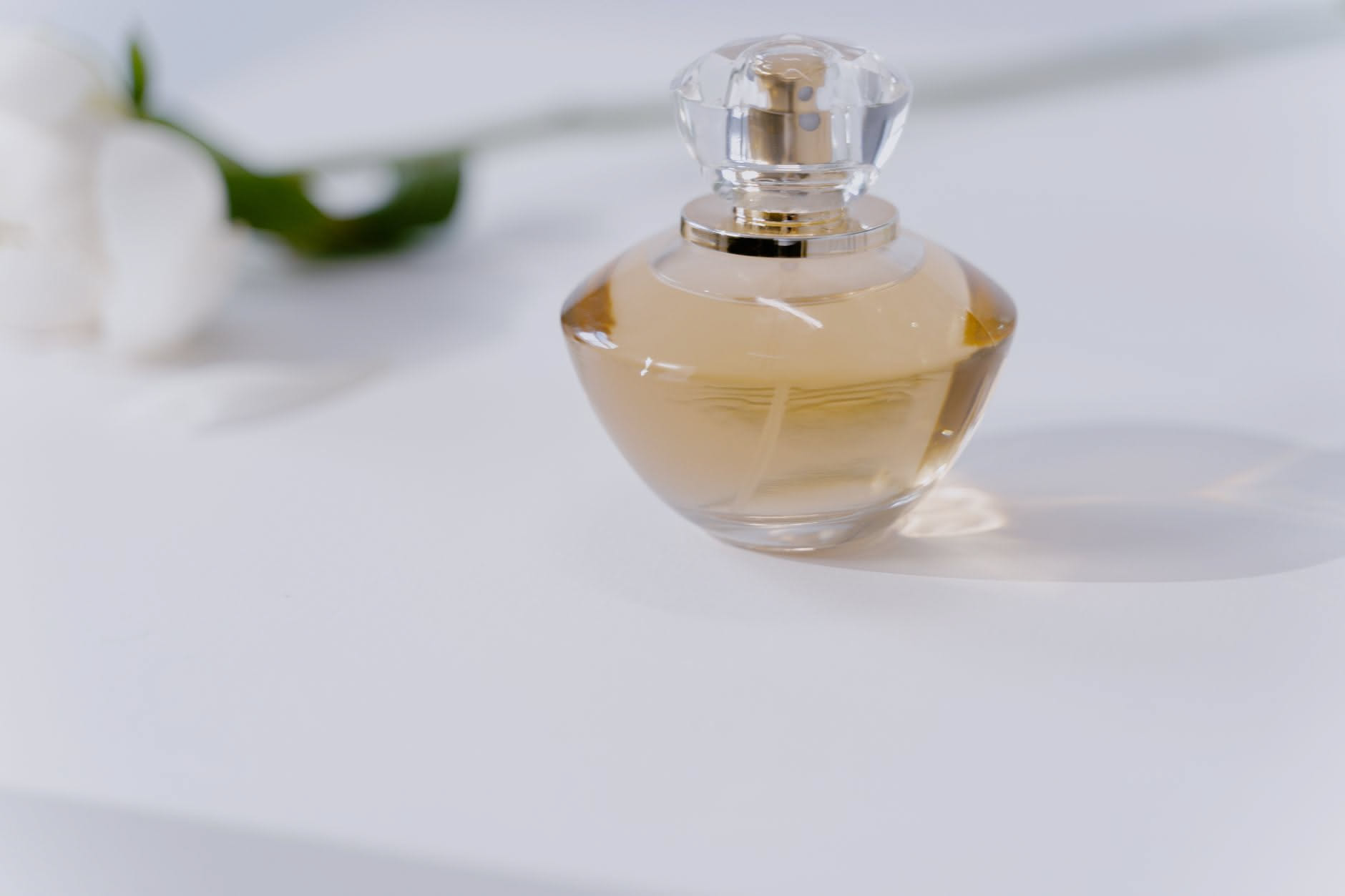 Flacone di profumo con spruzzatore davanti a uno specchio, con luce naturale che illumina il liquido ambrato trasparente all'interno