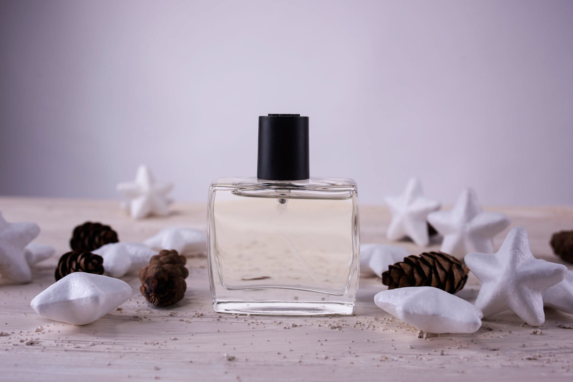 Due bottiglie di profumo di diversa forma e colore su uno sfondo bianco neutro, con gocce di fragranza riflesse dalla luce naturale