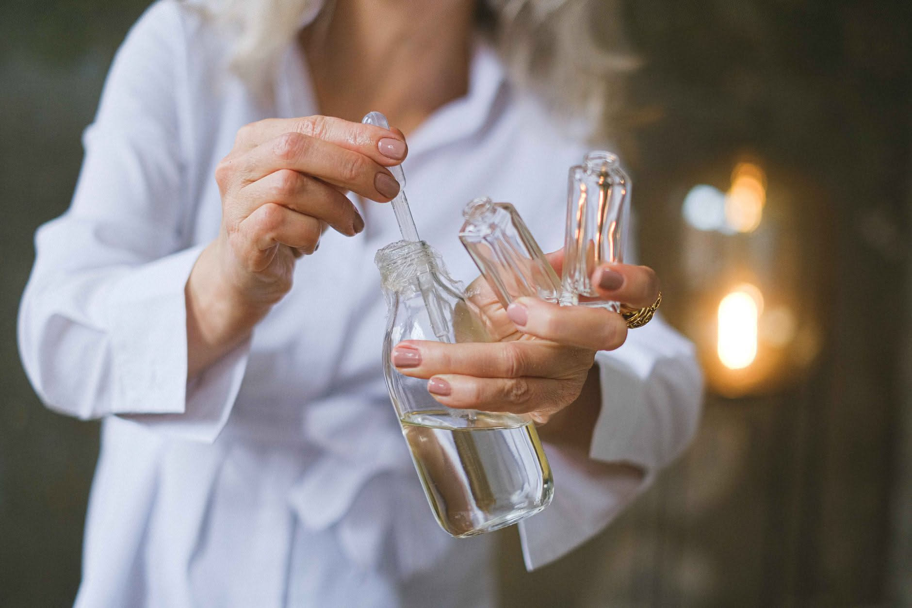 Flacone di profumo con spruzzatore su sfondo bianco, con gocce di liquido che riflettono la luce e un'aura di trasparenza attorno al vetro