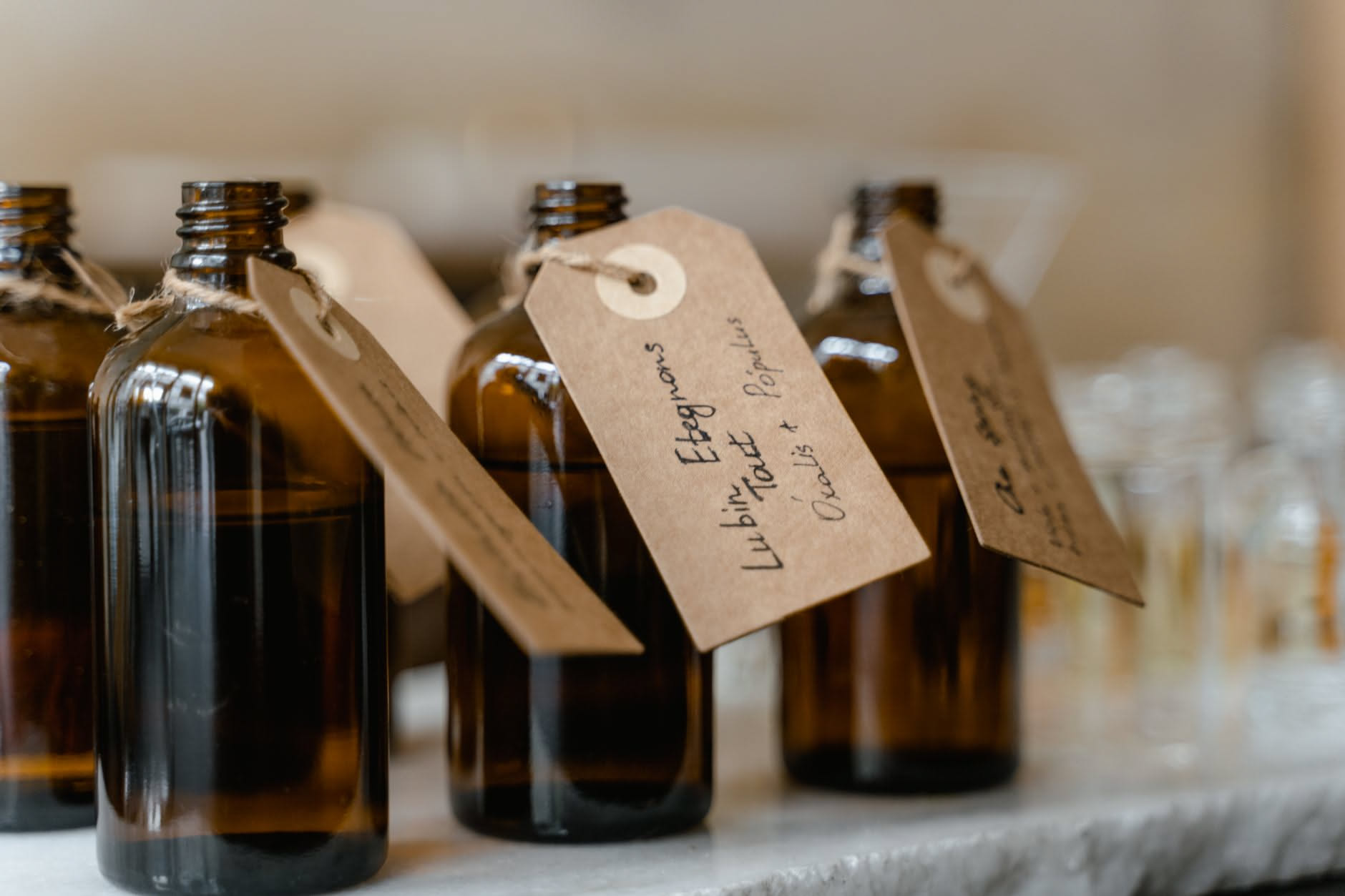 Mano di donna che regge una mouillette di carta bianca con profumo, posta davanti a bottiglie di profumi colorate in una profumeria