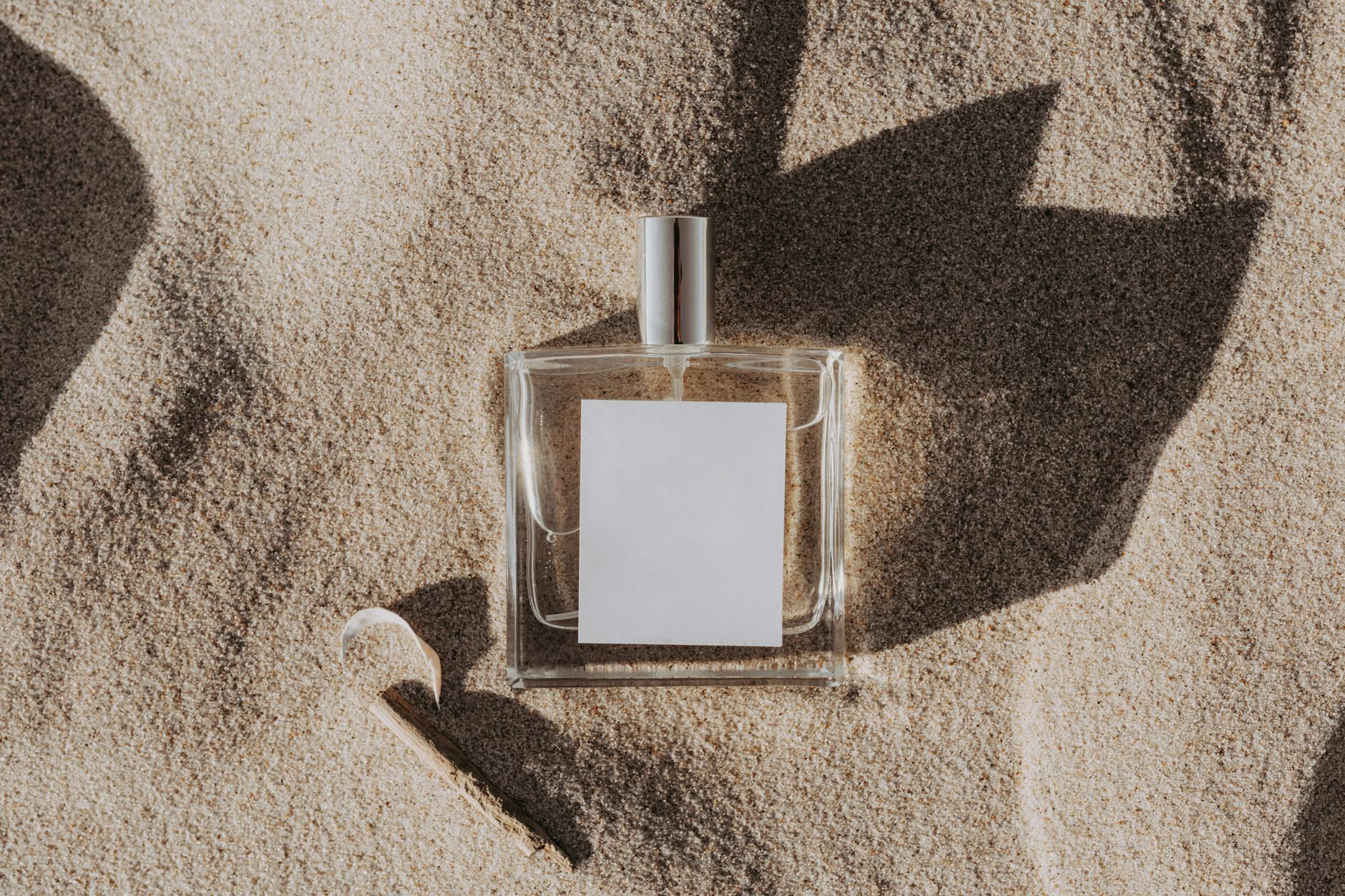 Primo piano di due polsi diversi con il polso sinistro che mostra una goccia di profumo trasparente, sfondo sfumato bianco e beige