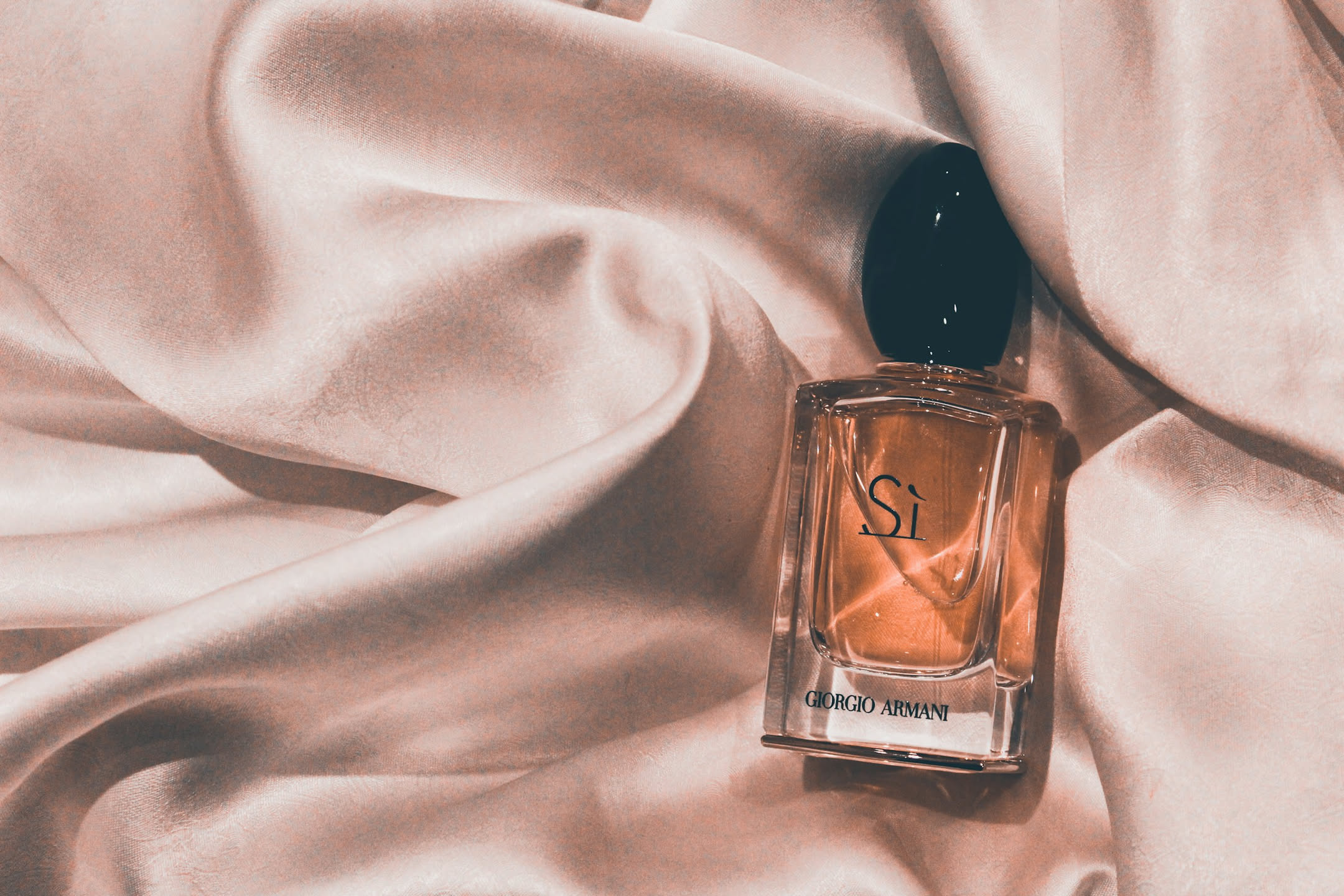 Piccolo imbuto di vetro e flaconcino da viaggio appoggiati su un piano chiaro accanto a un flacone di profumo